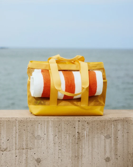Yellow bag with rolled-up orange and white towel on a concrete ledge by the sea.