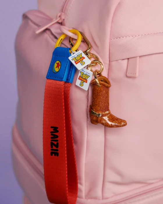 Keychain with cowboy boot and red strap attached to a pink bag