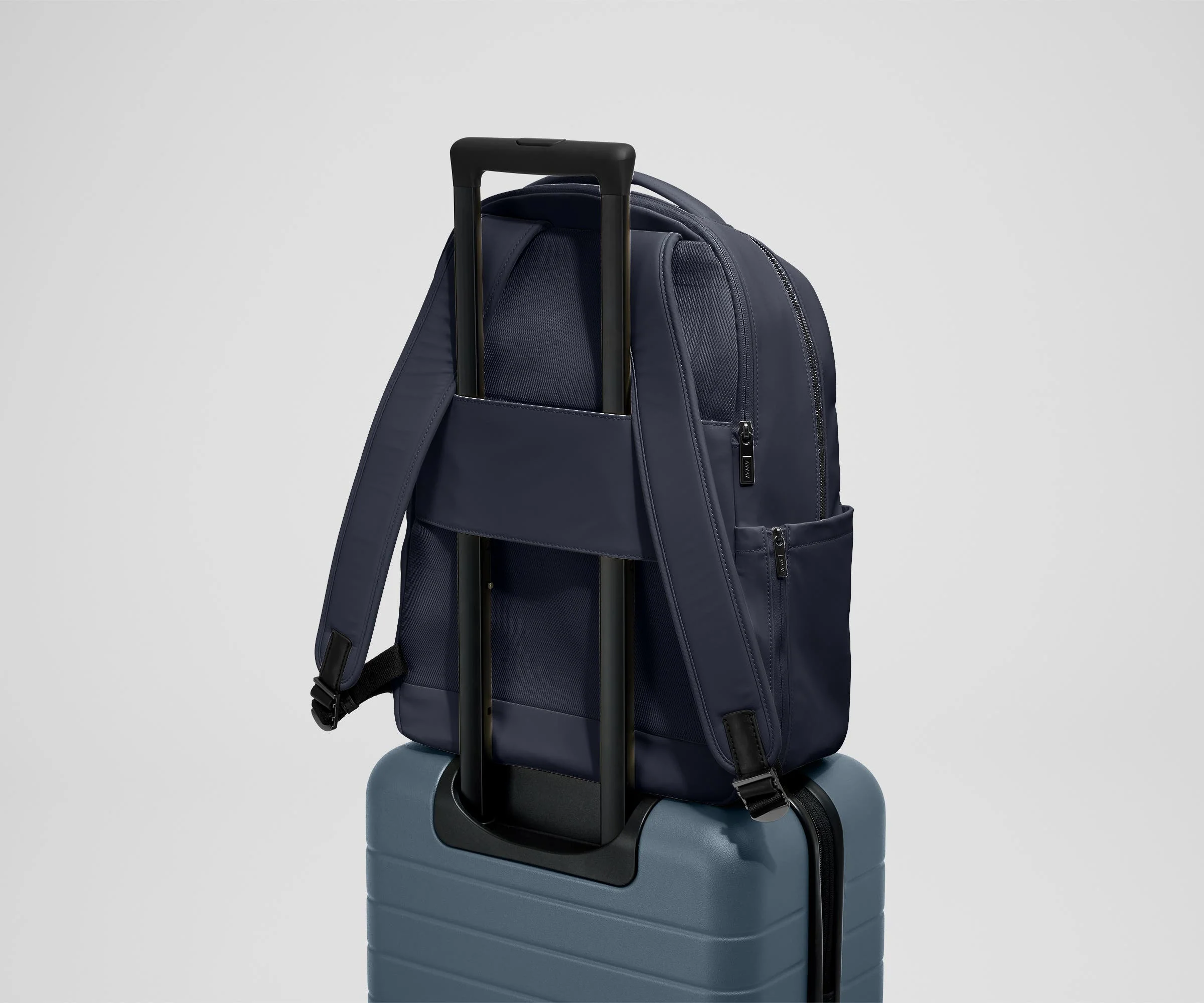 The Commuter Backpack on top of an Away suitcase, attached by the trolley pass-through sleeve