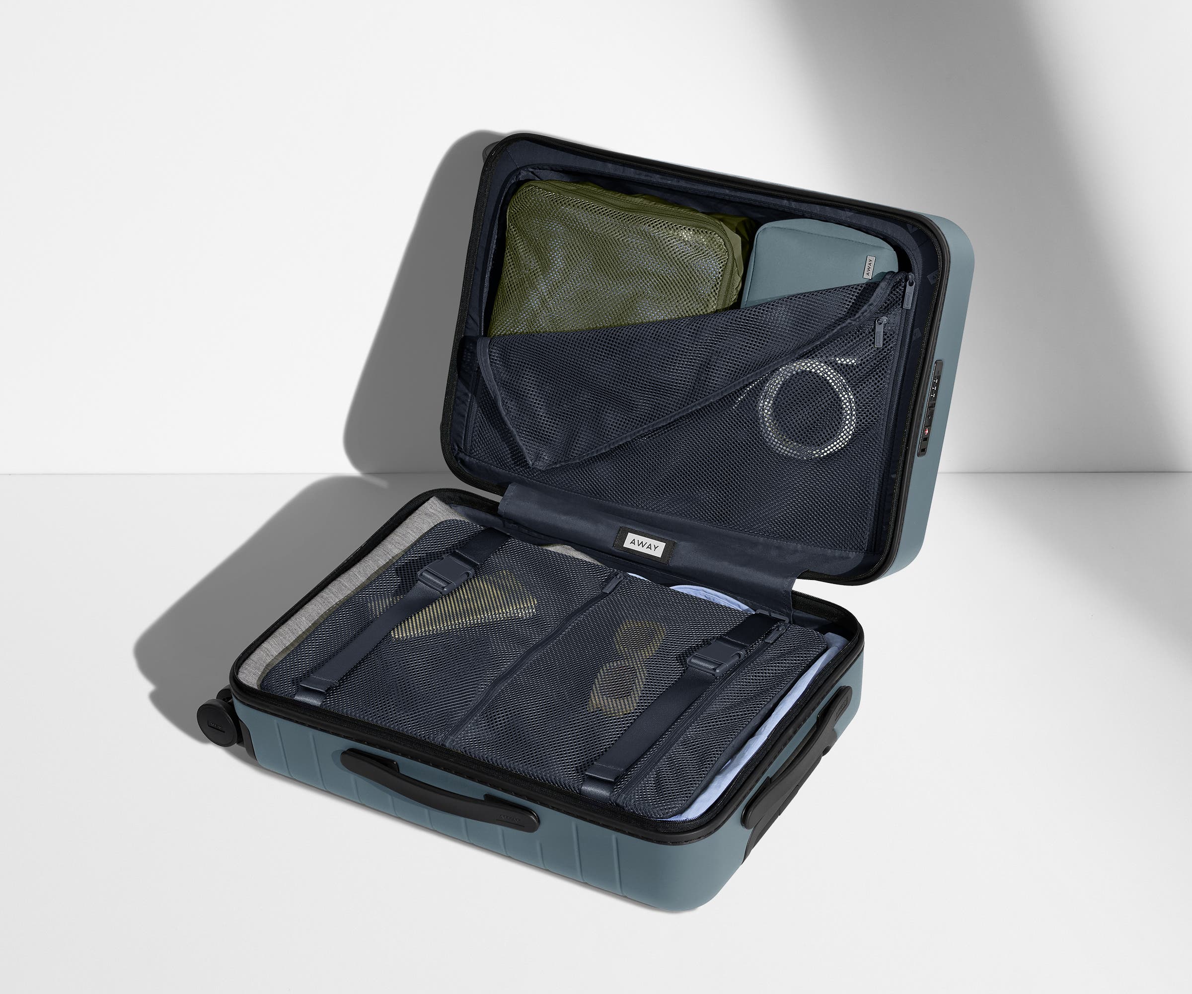 The Carry-On suitcase in Coast Blue shown open on its side and packed with Away's packing organizers to show capacity and the interior compression system, designed to help you pack more in