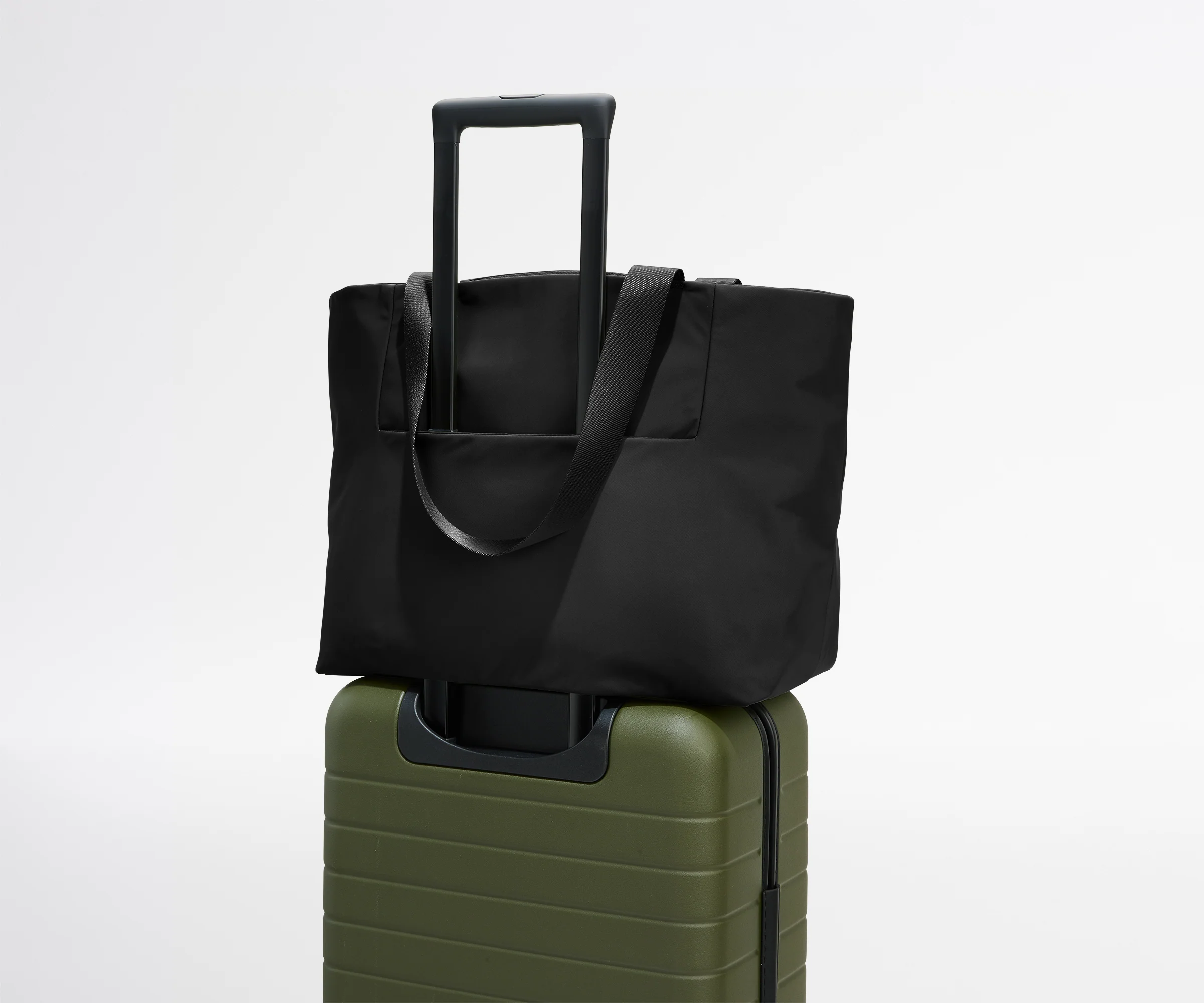 Black tote bag on top of a green suitcase against a white background