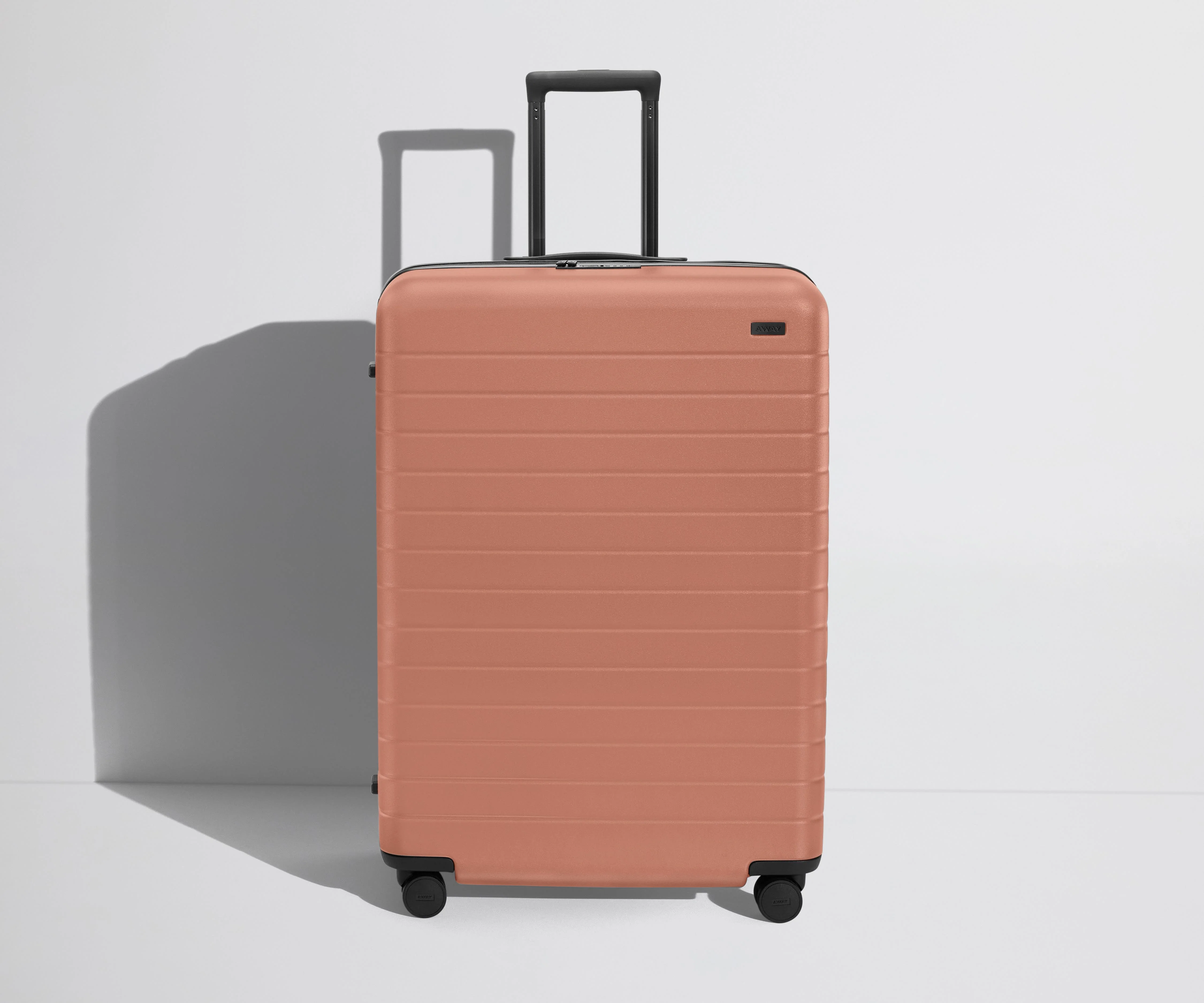 Front product view of The Large Flex suitcase in Clay Pink with raised handle