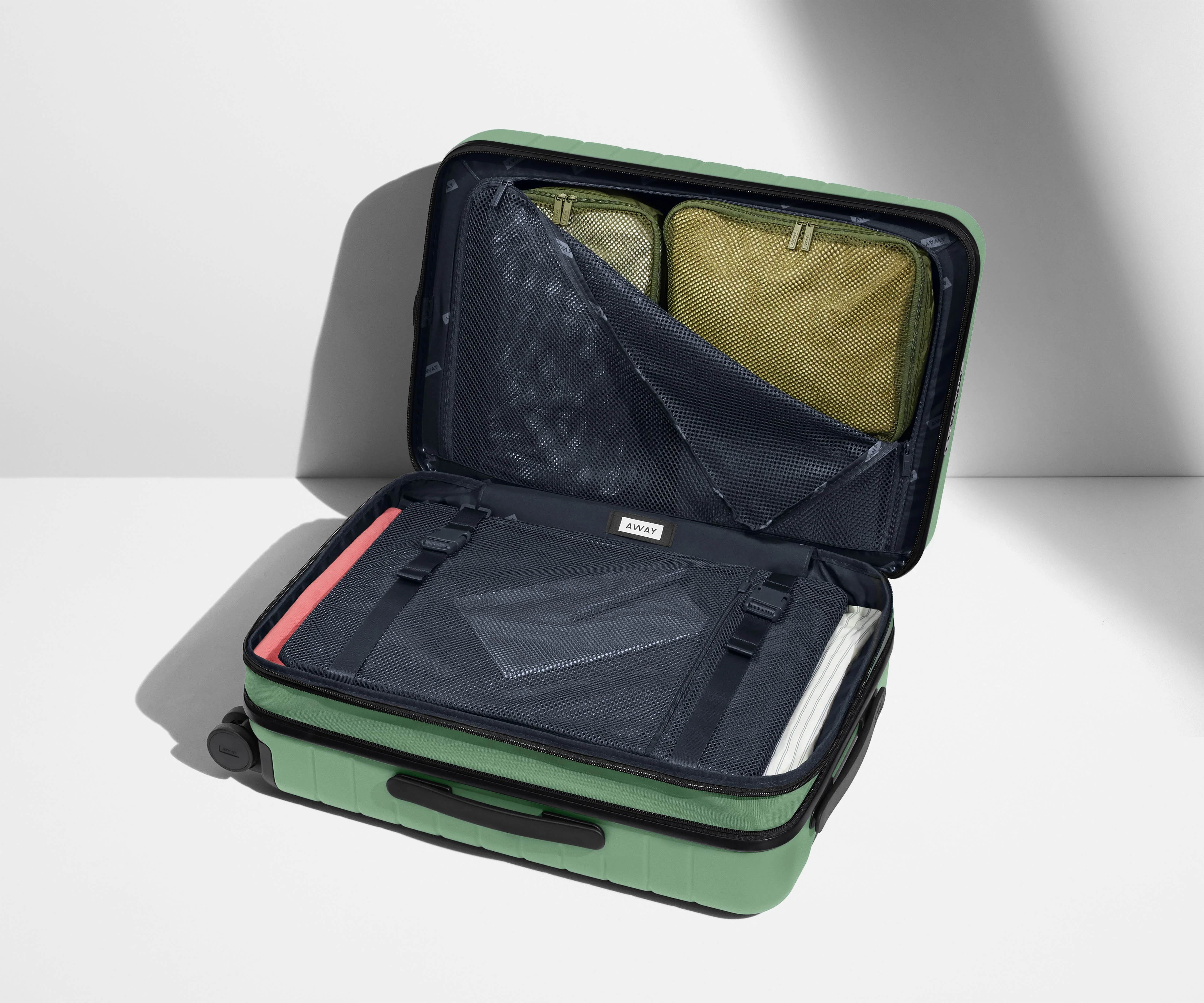 The Carry-On Flex suitcase in Sea Green shown open on its side and packed with Away's packing organizers to show capacity and the interior compression system, designed to help you pack more in