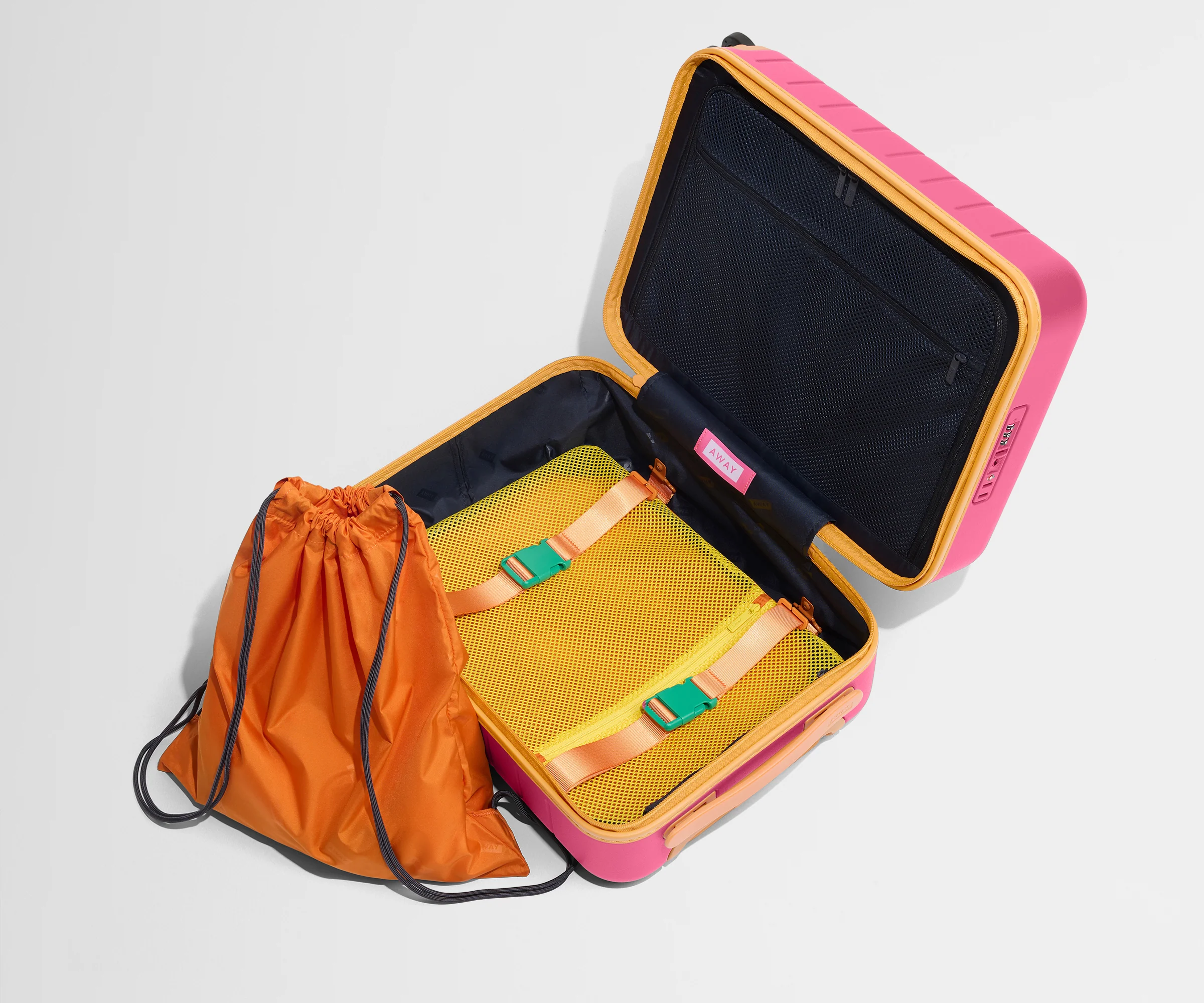 The Kids Carry-On suitcase in Cotton Candy Pink shown open and empty on its side to show capacity, and an orange laundry bag can double as a backpack for smaller travelers.