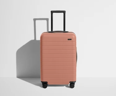Front product view of The Bigger Carry-On suitcase in Clay Pink with raised handle