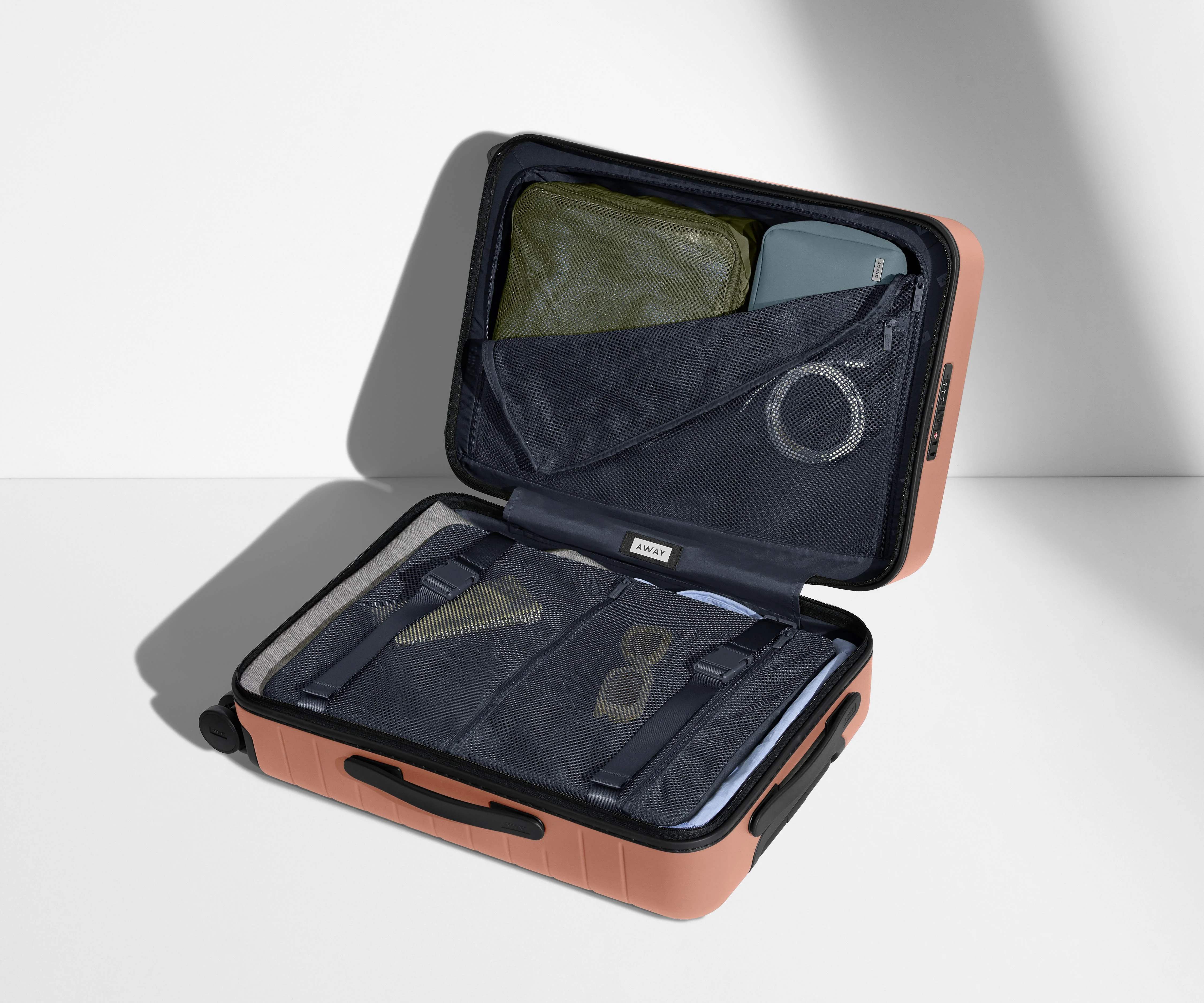 The Carry-On suitcase in Clay Pink shown open on its side and packed with Away's packing organizers to show capacity and the interior compression system, designed to help you pack more in