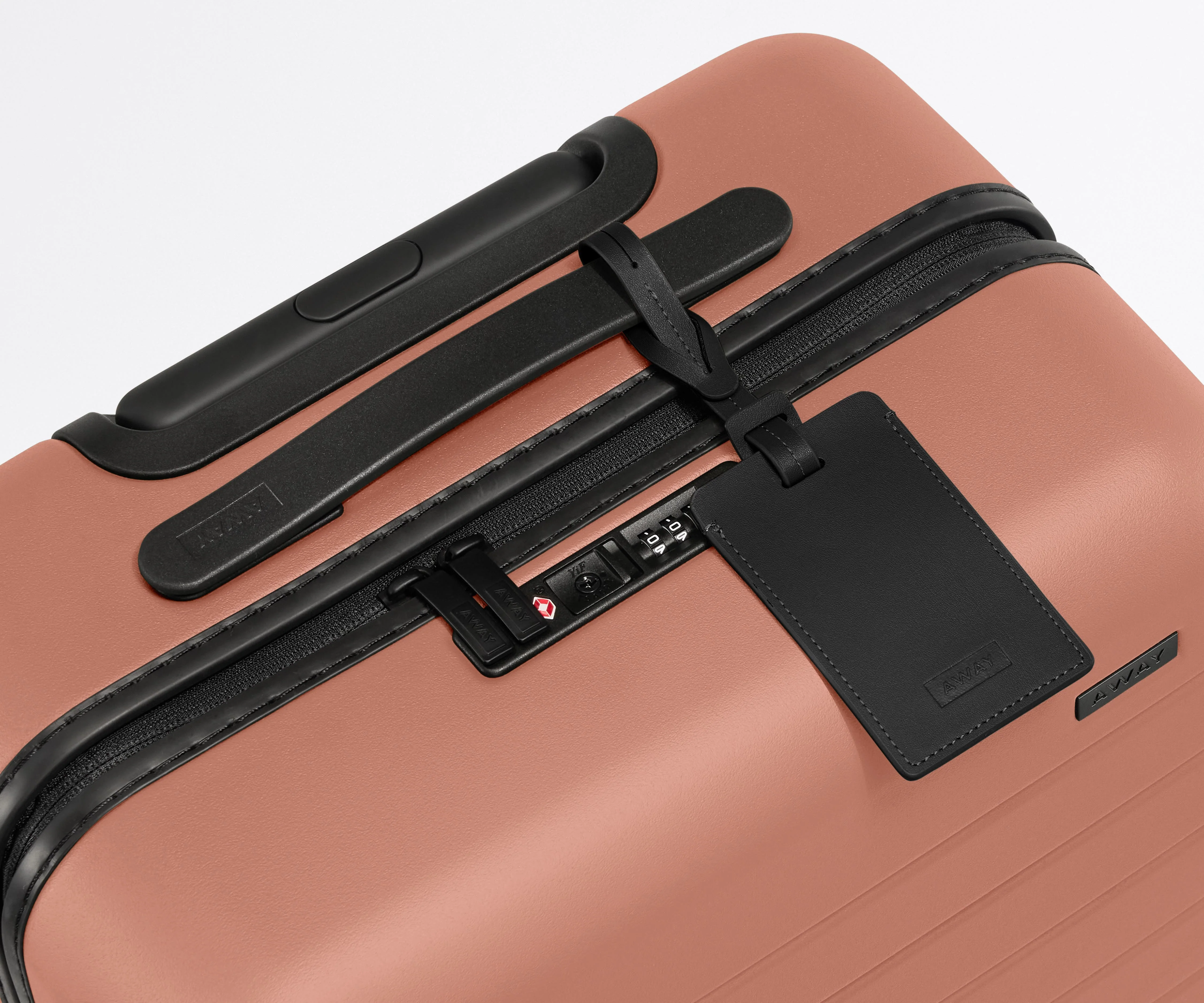 The Carry-On suitcase in Clay Pink shown shown from above highlighting TSA-approved combination lock and recycled leather luggage tag