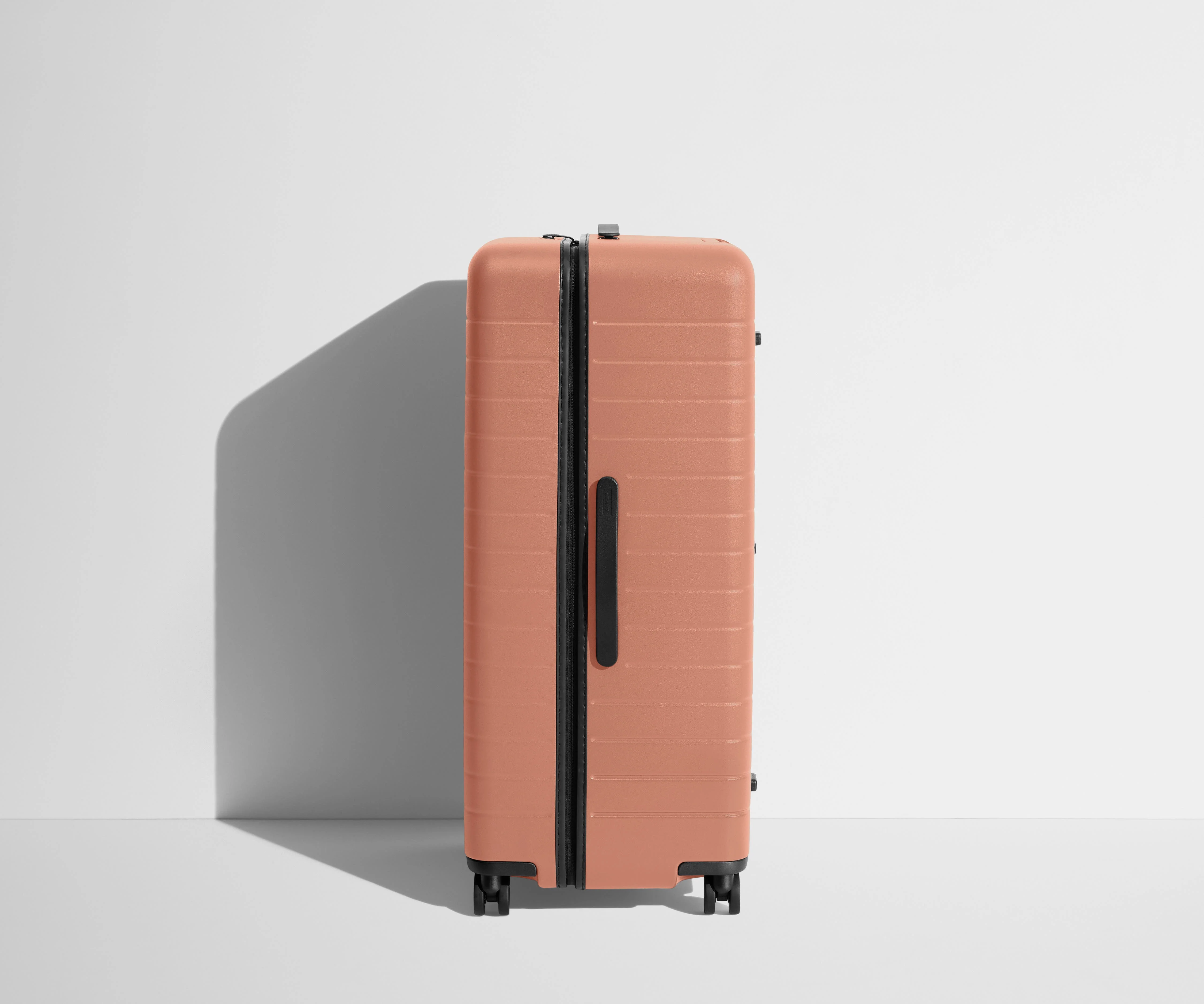 Side product view of The Trunk suitcase in Clay Pink to show the slimmer top lid and deeper main compartment for easy access and packing