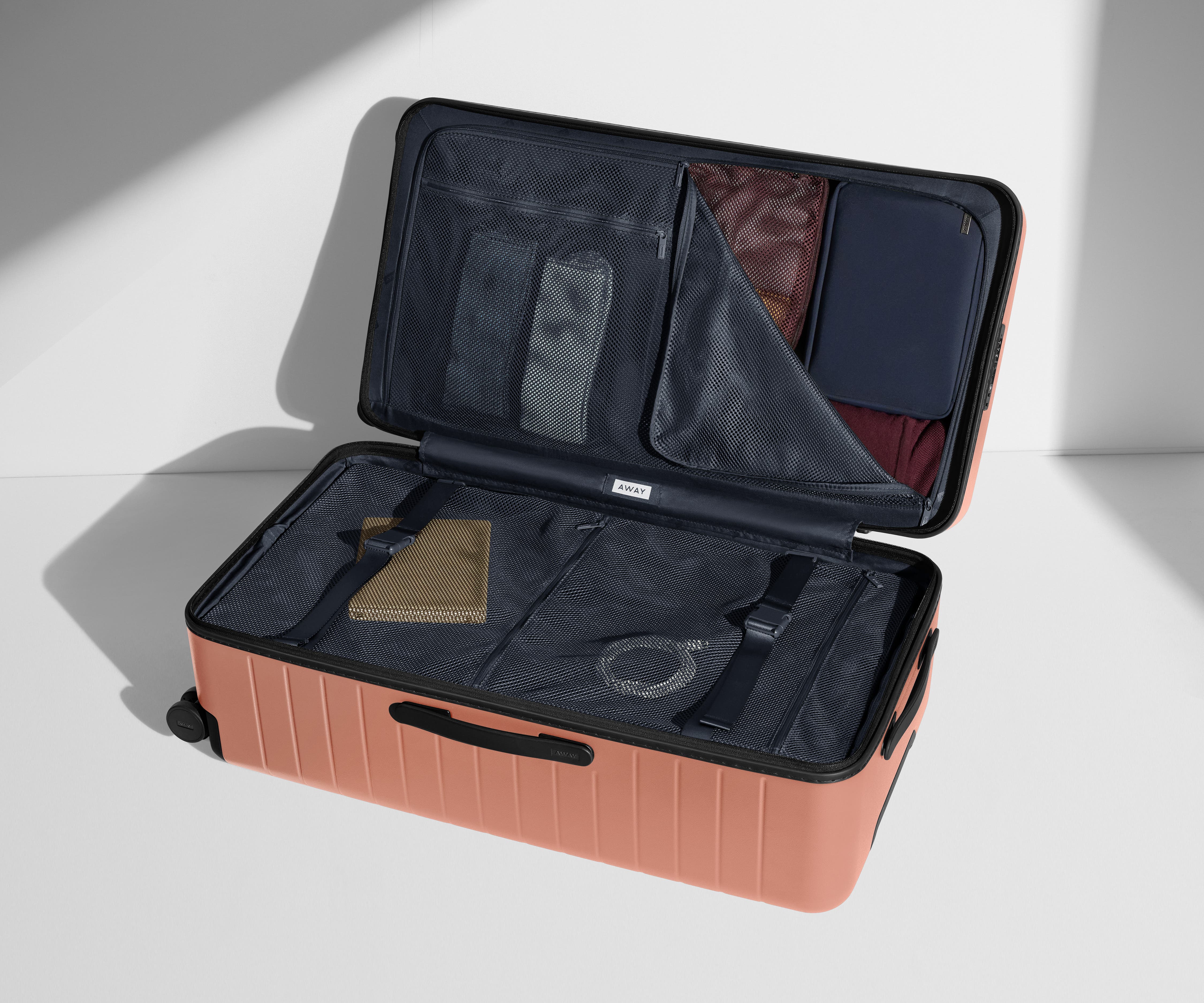 The Trunk suitcase in Clay Pink shown open on its side and packed with Away's packing organizers to show capacity and the interior compression system, designed to help you pack more in