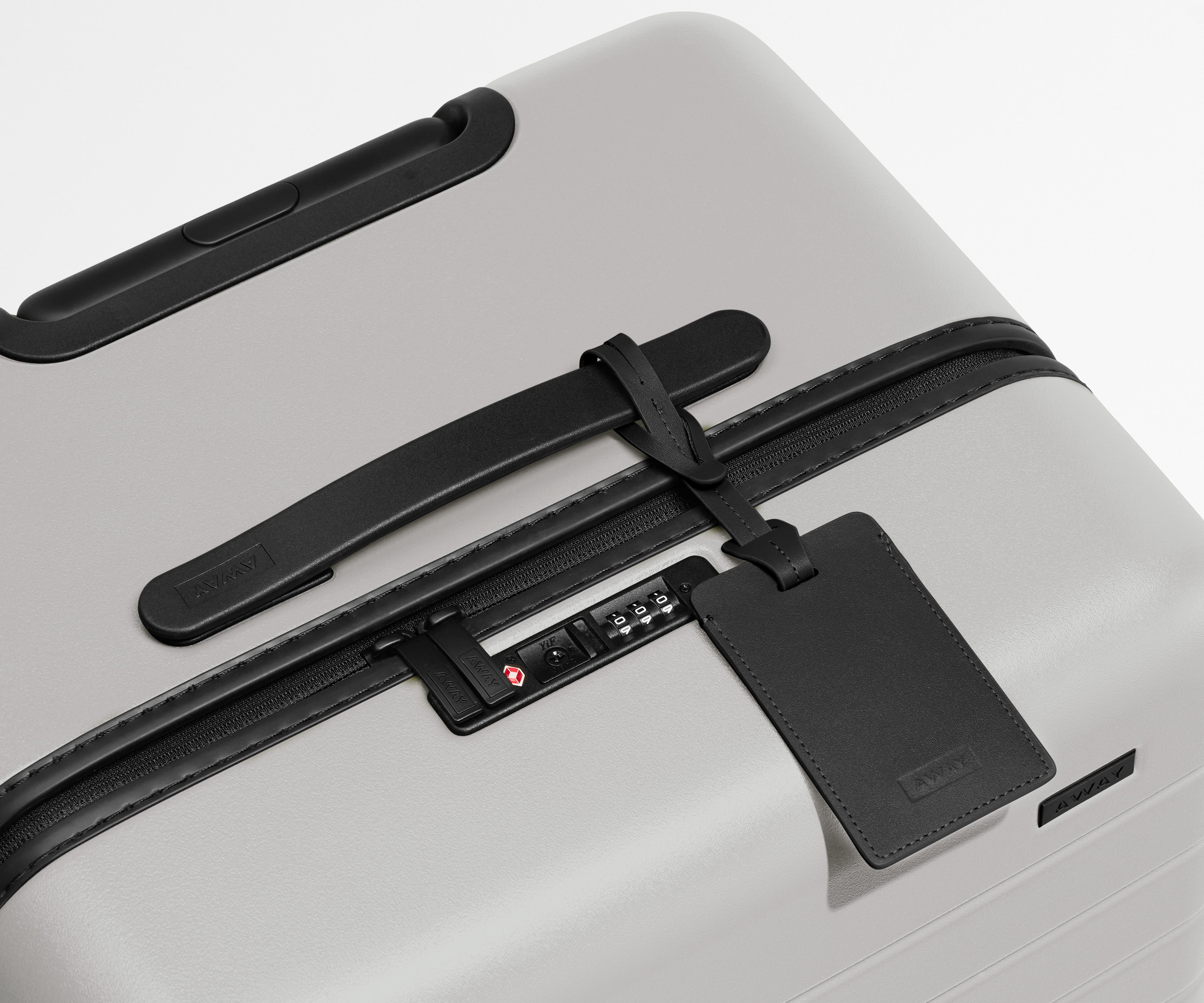The Trunk suitcase in Cloud Gray shown shown from above highlighting TSA-approved combination lock and recycled leather luggage tag