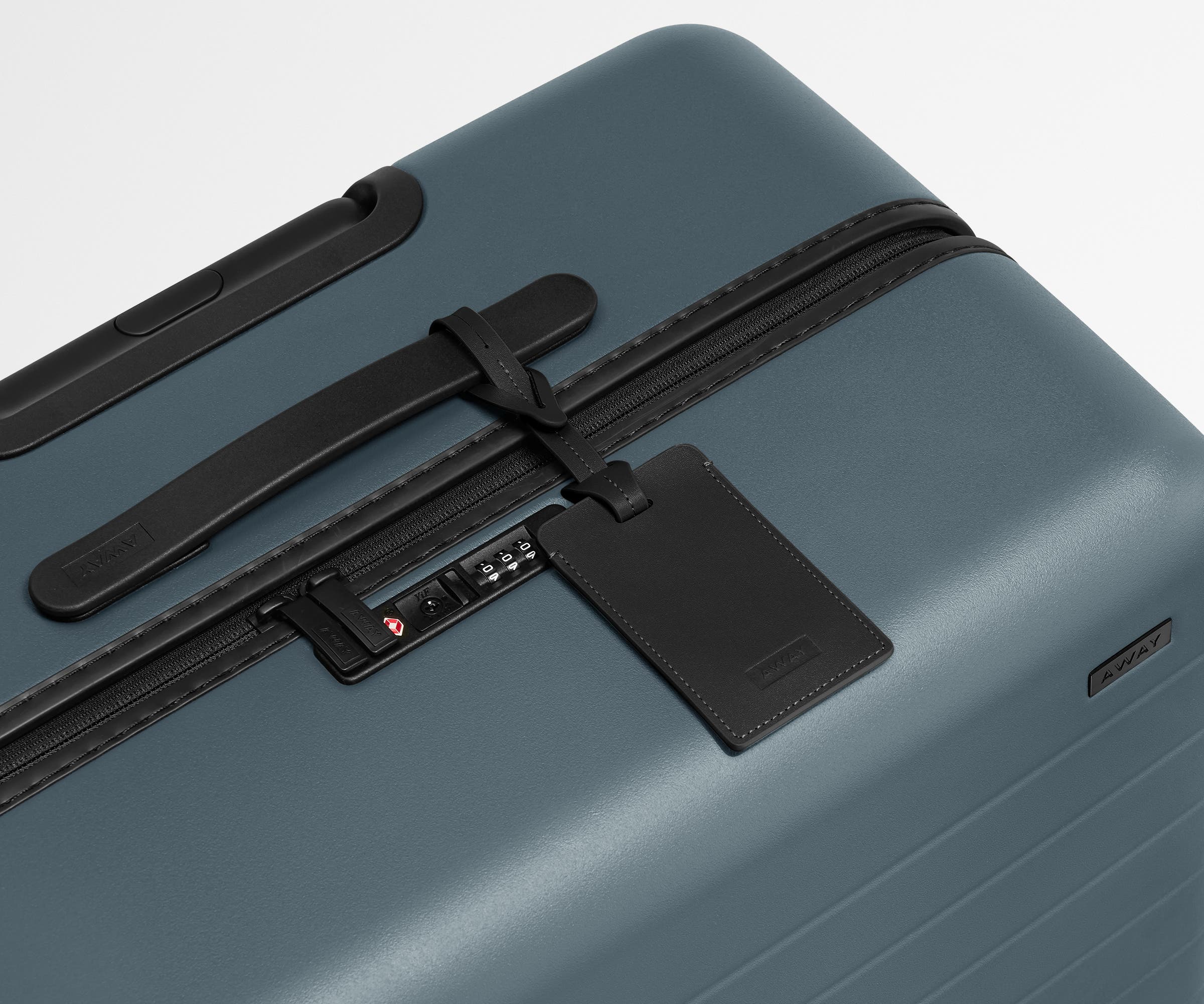 The Large suitcase in Coast Blue shown shown from above highlighting TSA-approved combination lock and recycled leather luggage tag