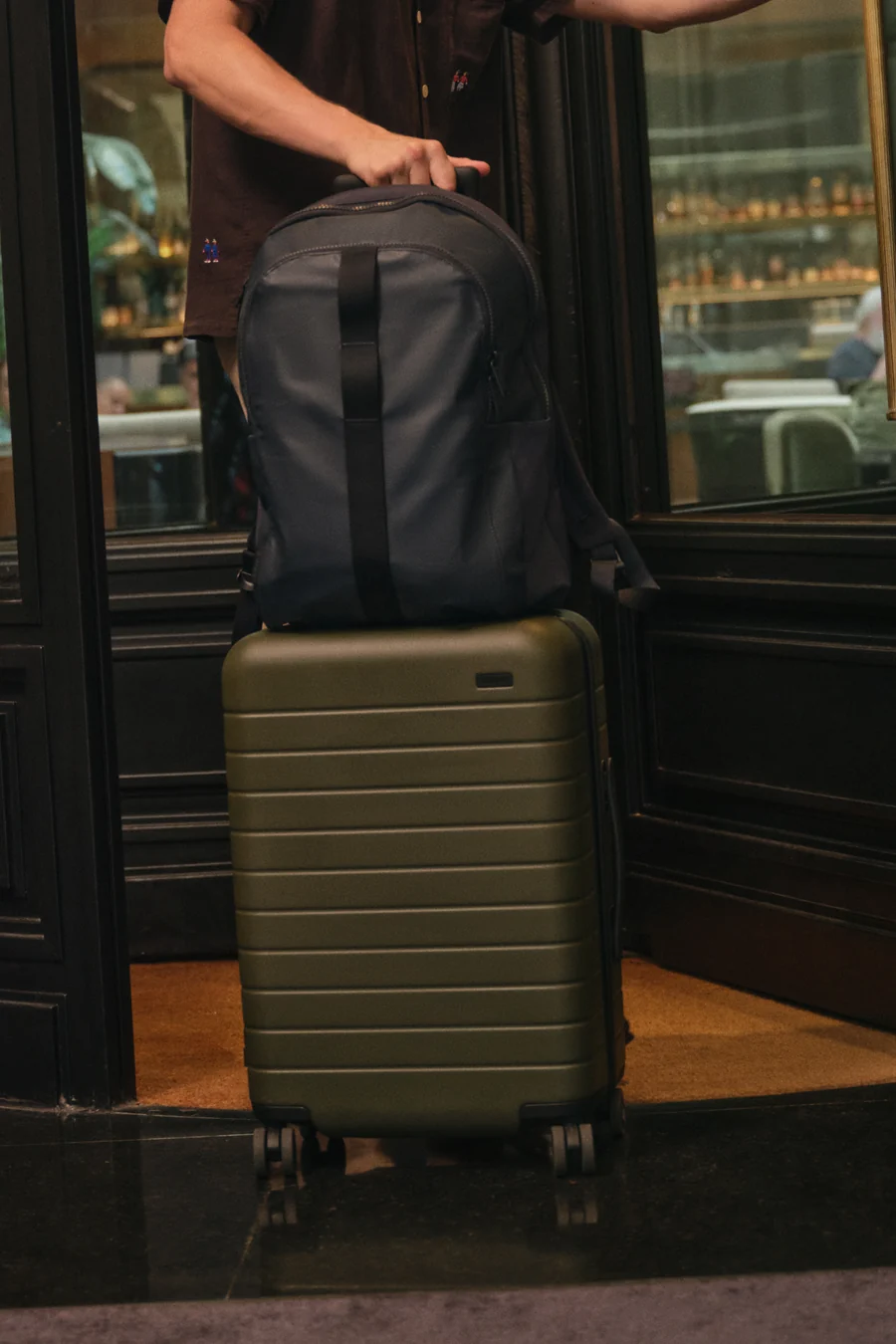 Person holding a backpack on top of a suitcase in a doorway.