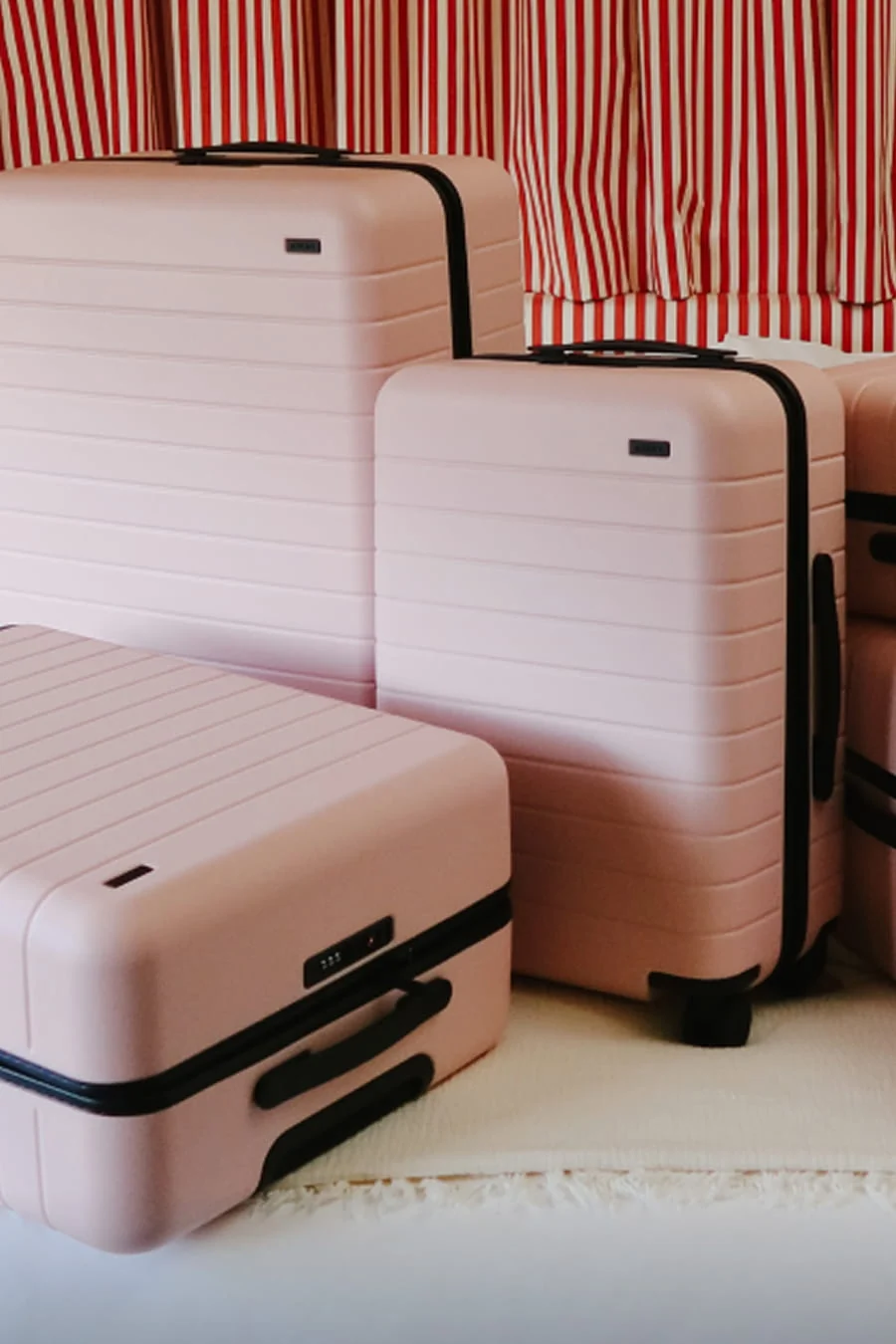 Set of pink suitcases with black handles against a red and white striped background