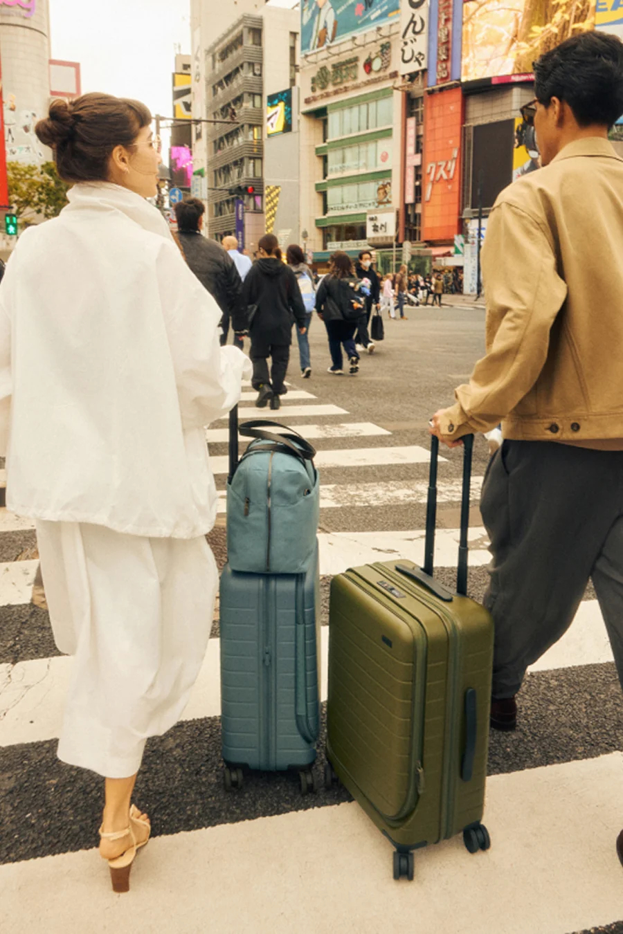 Two people with suitcases crossing a street in an urban setting