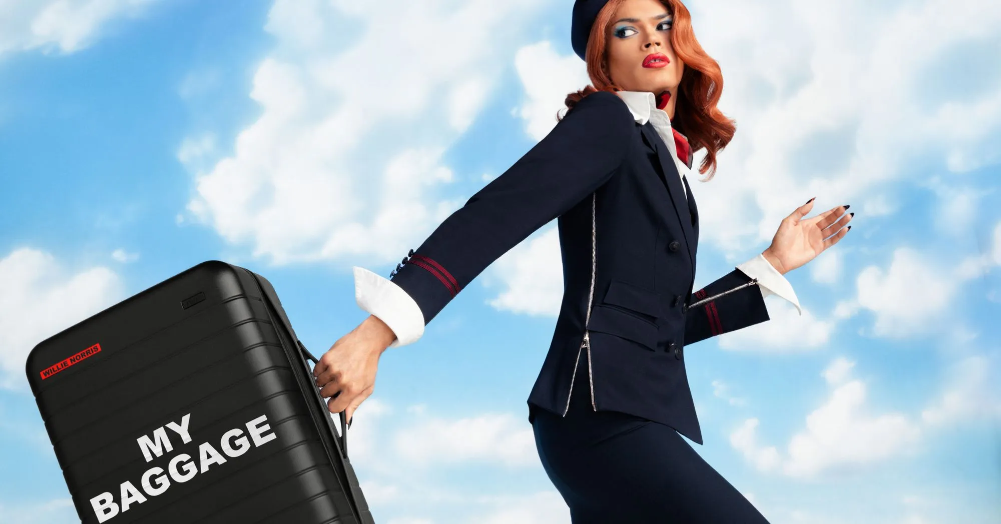 West Dakota posing with a black Away suitcase against a blue cloudy sky background